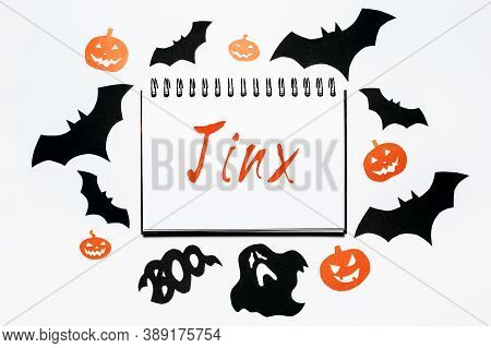Happy Halloween Holiday Concept. Notepad With Text Jinx On White Background With Bats, Pumpkins And 