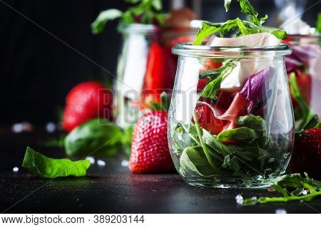 Summer Salad With Arugula, Soft Cheese, Red Strawberry And Prosciutto In Glass Jars On Black Table, 