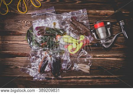 Spinning Rod With A Reel And Silicone Baits In Plastic Bags. Studio Photo On A Wooden Background. Fl