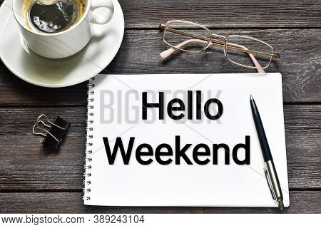 Hello Weekend. It Is Written In A Notebook Next To Glasses, A Pen And A Cup Of Coffee On A Wooden Ba