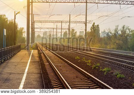 Modern Multi-track Railway In Backlit Sunlight On A Background Of Distant Urban Structures