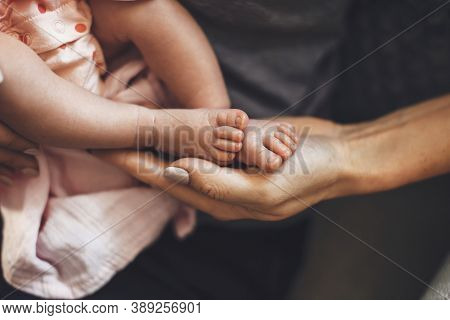 Caucasian Parent Holding His Newborn Daughter Feet In Hand While She Is Sleeping