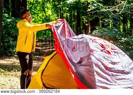 African American In Yellow Jacker Putting On A Tent In Forest
