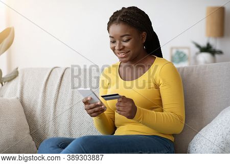 Online Shopping. Smiling Black Lady Using Smartphone And Credit Card At Home, Browsing Mobile Bankin