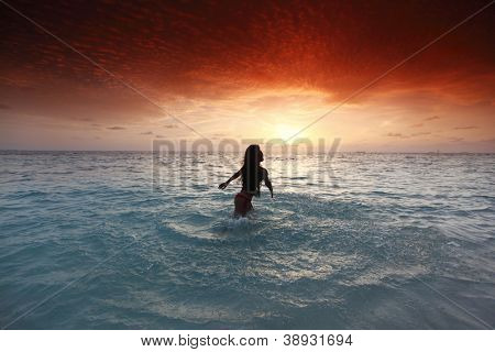 Vrolijke vrij jonge vrouw splashin in zee op zonsondergang