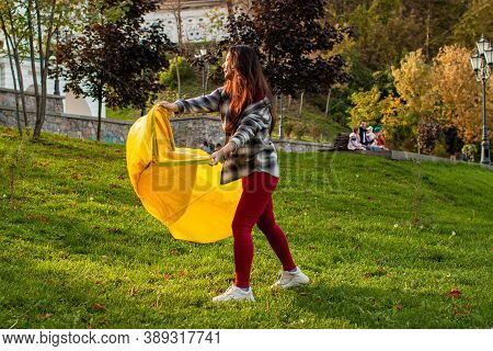 A Young Woman Inflates A Yellow Lamzac With Air. A Woman Inflates An Air Sofa In Park.