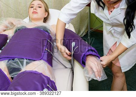 A Beautician With Dark Hair Prepares A Young Woman For The Pressotherapy Process. Wearing A Special 