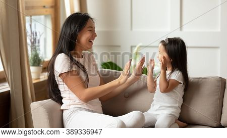 Smiling Young Mother And Little Daughter Clapping Hands On Couch