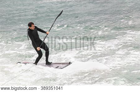 Surfer On Sup Stand Up Paddle Board On Dark Wave. Winter Surfing In Sea. Side View Of A Man Falling 