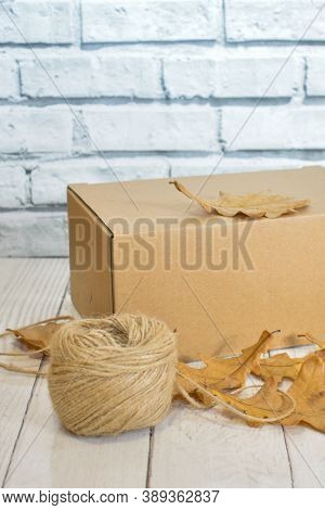 Cardboard Box, Autumn Oak Leaves And A Ball Of Rope On The Background Of A Wooden Table Top And A Li