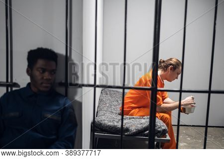Dinner In A Prison Cell. A Prisoner Eats Tasteless Food From An Iron Bowl Under Guard Behind Bars