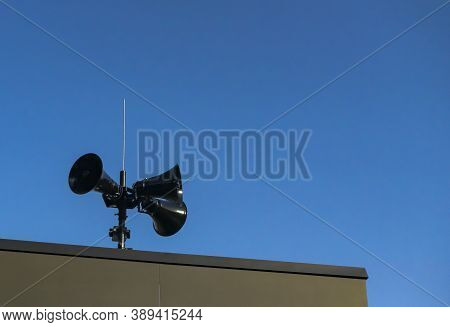 Three Black Modern Megaphones Loudspeaker On The Building Roof Over Bluue Sky