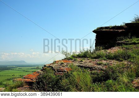 The Top Of A Stone Mountain With Steep Cliffs Overgrown With Grass Overlooking A Picturesque Valley.