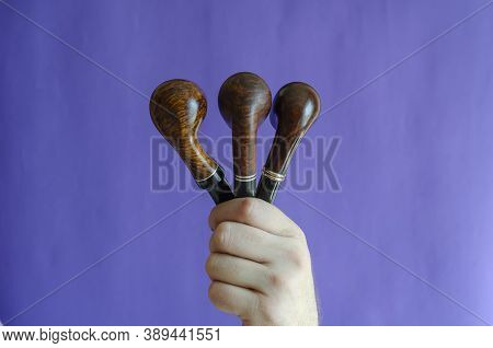 A Male Hand Holds Three Smoking Pipes On A Blue Background. Occasional Smoking Pipes Bend From Heath