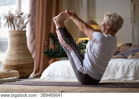 Active Senior Woman Doing Yoga Training At Home, Holding Navasana Or Boat Yoga Pose