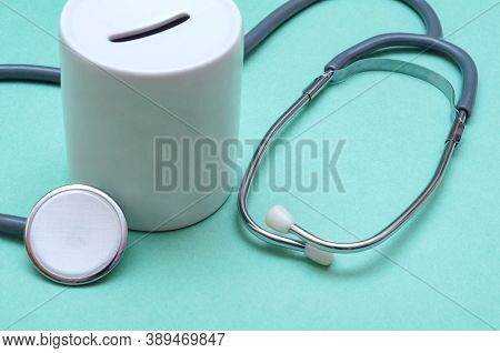 Cost Of Healthcare. Money Box With A Medical Doctors Stethoscope On Green Background