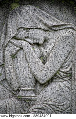Sad Woman Careved Into Tombstone Cradles An Urn. Full Frame In Natural Light.