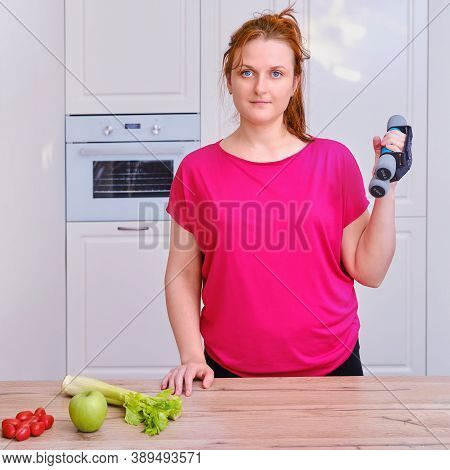 Young Woman In Home Kitchen With Dumbbells, Vegetables And Fruit. Concept Of Proper Nutrition And Sp