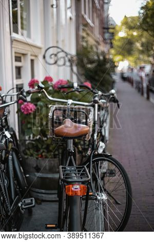 Black Bicycle With A Brown Seat And Red Fire On The Trunk Is Parked On A Street In Amsterdam With Pi