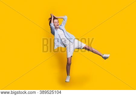 Smiling Caucasian Boy In Casual Clothes Is Jumping On A Yellow Studio Wall Touching His Long Hair