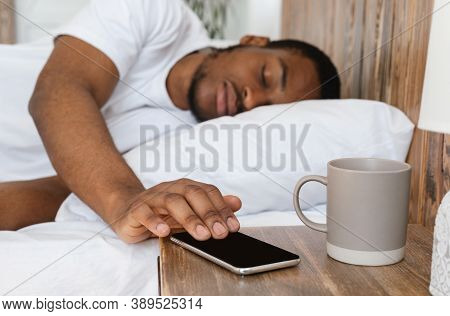 Asleep African American Man Sleeping Through Alarm Clock On Phone Lying In Bed In Bedroom At Home In