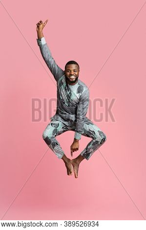 Excited Black Man In Traditional Grey Clothes Jumping Up Over Pink Studio Background, Full Length Ph