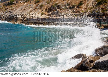 Sea Water Beats Against Rocky Rocks And Makes Waves With Foam, Rugged Pier In The Sea