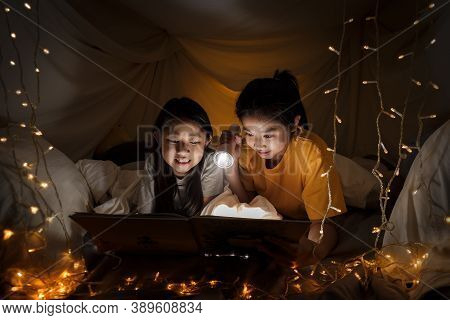 Family Concept. Elder Sister And Sister Reading Book With Flashlight Together Before Bedtime. Sister