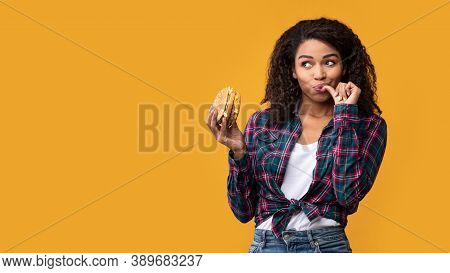 Cheat Meal. Portrait Of Happy African American Casual Woman Eating Tasty Burger, Licking Finger, Loo