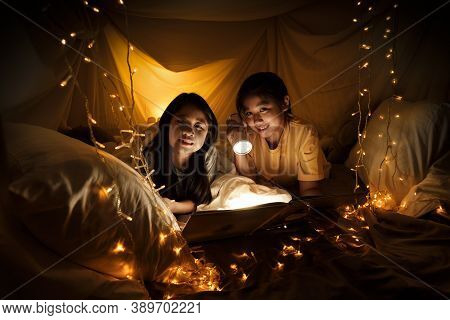 Family Concept. Elder Sister And Sister Reading Book With Flashlight Together Before Bedtime. Sister
