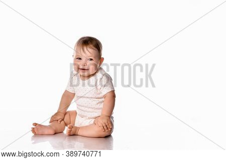 Shy Baby Girl Child Wearing Body Stretchie Sitting On Floor Looking At Camera. Newborn Infant Barefo