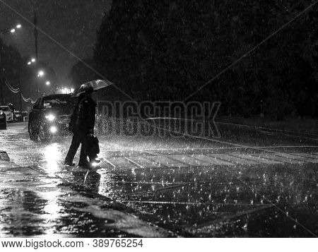 View Of A Pedestrian Crossing In The City At Night During A Heavy Downpour. Silhouettes Of People Wi