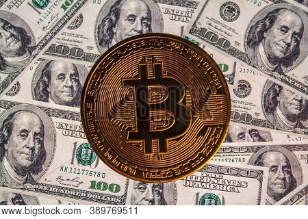 Bitcoin Coin Against The Background Of Us Dollars. A Lot Of American Money Dollars And Gold Bitcoin.