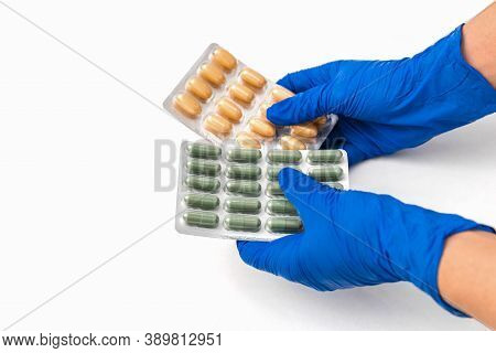 Close Up Hands With Blue Gloves On Holding Different Pills In Blisters On White Table. Prophylaxis A