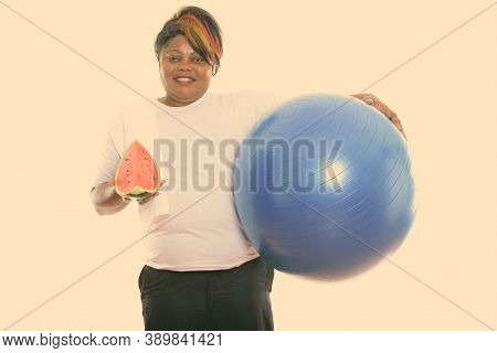 Studio Shot Of Happy Fat Black African Woman Smiling While Holding Exercise Ball And Slice Of Waterm