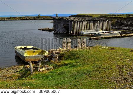 Old White Yellow Rusty Iron Boats On Green Grassy Shore Of Round Bay, With Wood Barn On The Water. L