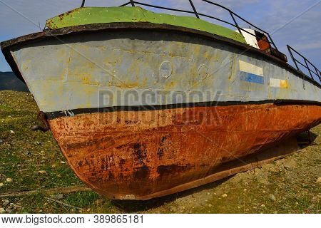 Red Gray Bottom Of Ship, Old Rusty Abandoned Boat Lie On Green Grassy Shore In The Light Of The Suns