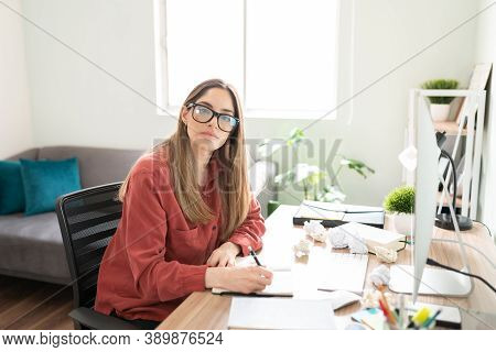 Uninspired Female Writer And Author Making Eye Contact While Trying To Get Inspired In Her Office Ne