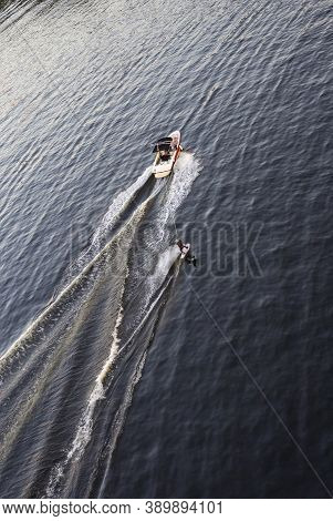 Speedboat Towing An Athlete On A Board Against The Background Of The Forest. Athlete Water Skiing An