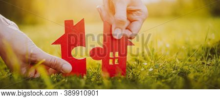 Red House On Green Grass On A Sunny Day. Model Of Home With A Shape Of Two Parts Of Puzzle In Human 