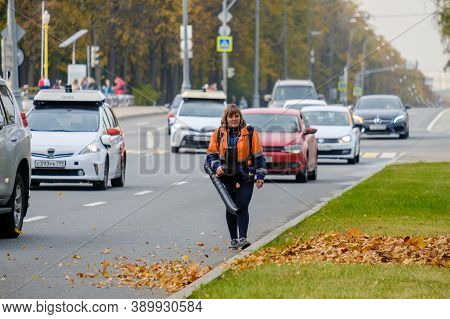 Moscow. Russia. October 11, 2020 A Woman Utility Worker Uses A Blower To Remove Fallen Leaves On A C