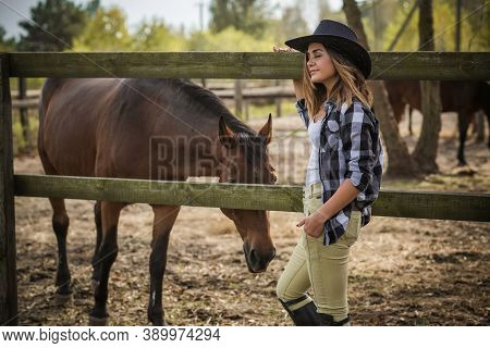 American Woman On A Horse Farm. Portrait Of Girl In Cowboy Hat With A Horses. Hippotherapy At Nature