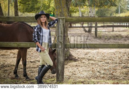 American Woman On A Horse Farm. Portrait Of Girl In Cowboy Hat With A Horses. Hippotherapy At Nature