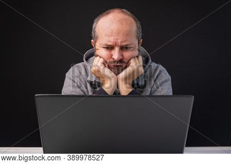 Man In Hoodie Working From Home Office, Worried Face Expression. Adult Bearded Man Sitting Behind Co