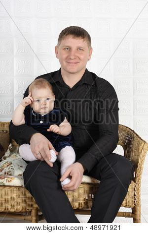 Happy Young Father And His Little Cute Baby Sit On Wicker Sofa.