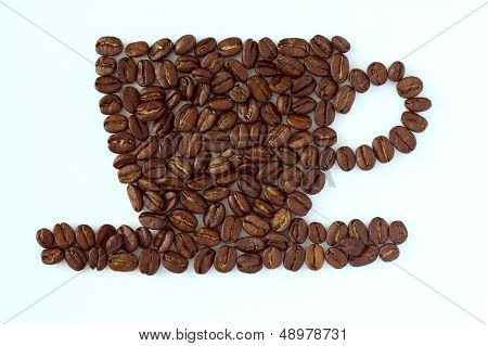 Roasted coffee beans layed in the shape of a cup and saucer