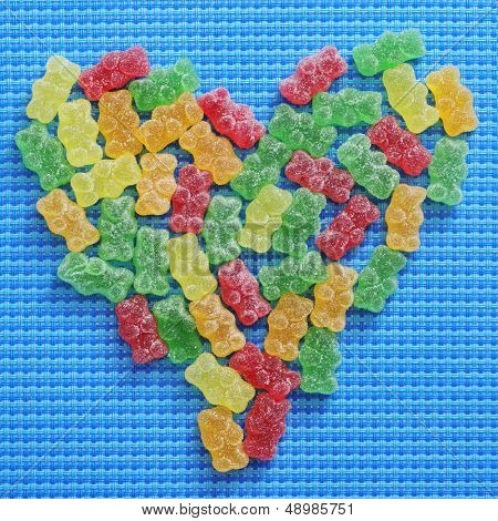 Gummibärchen in verschiedenen Farben bilden ein Herz auf blauem Hintergrund gewebte
