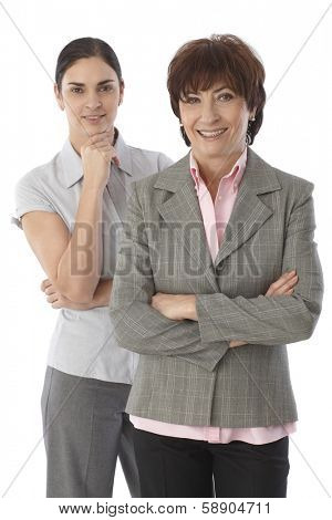 Two women of two generations standing arms crossed, smiling happy, looking at camera.