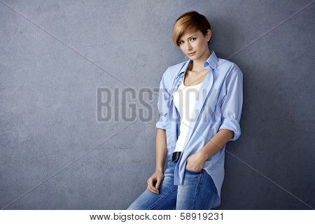Casual young woman leaning to wall, hand in pocket