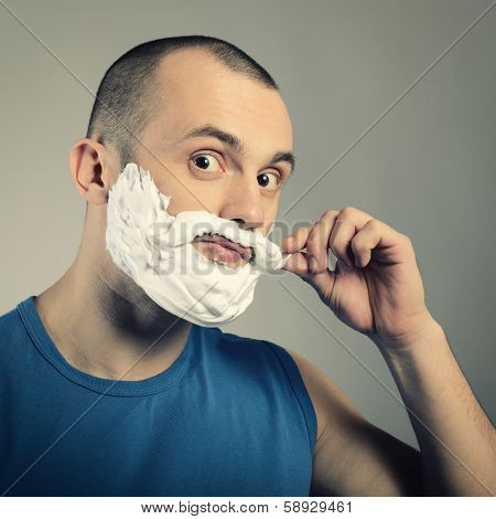 Funny portrait of trendy man making moustache and beard of shaving foam, toned.